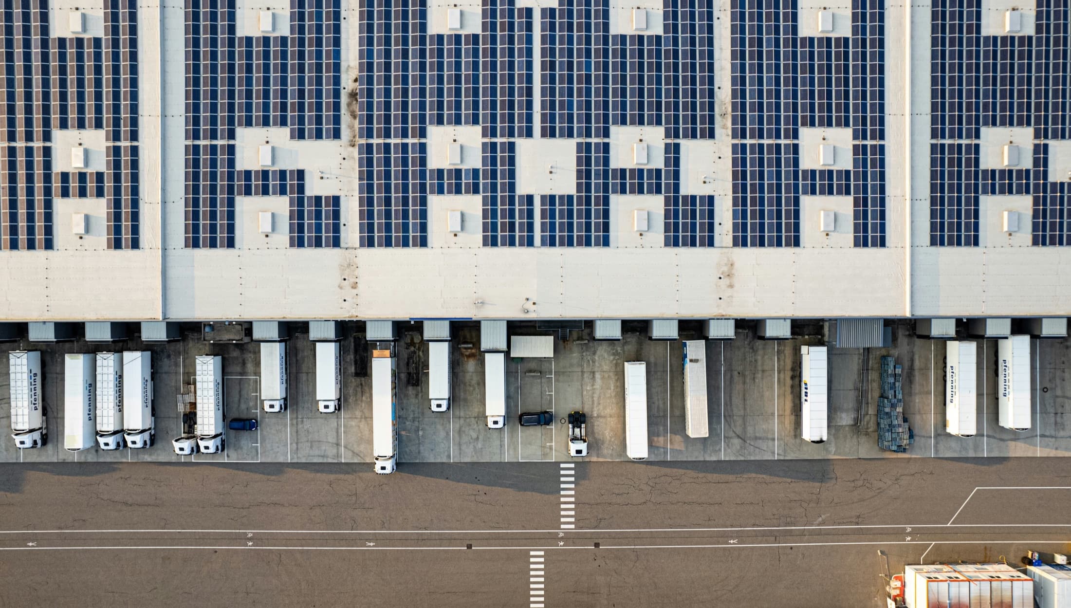 Aerial view of a modern logistics warehouse with solar panels, loading docks and parked trucks